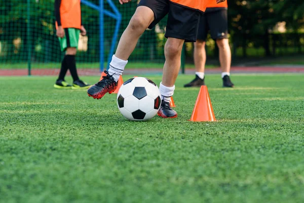 Close up adolescente em sportswear treina futebol no estádio e aprende a circular a bola entre treinar cones laranja. — Fotografia de Stock