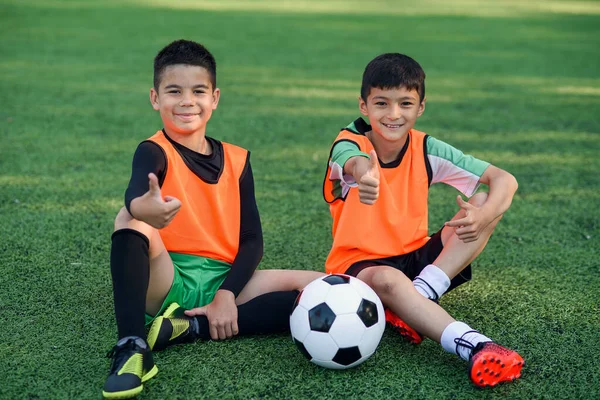 Joyful adolescente jogadores de futebol masculino mostrar ok sinal descansando no relvado artificial do campo de futebol após o treinamento intensivo. — Fotografia de Stock