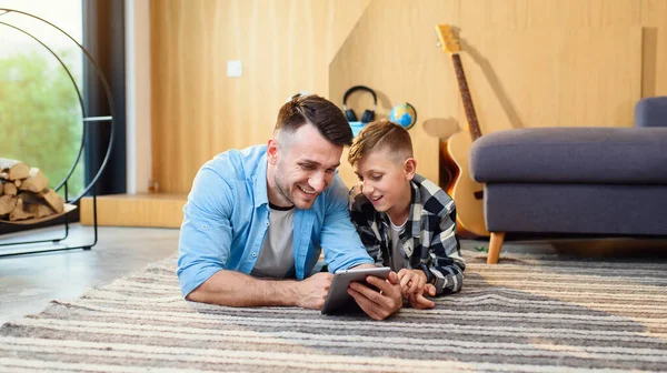 Niño con el padre acostado en el suelo usando tableta PC en el apartamento moderno. Feliz tiempo en familia juntos. — Foto de Stock