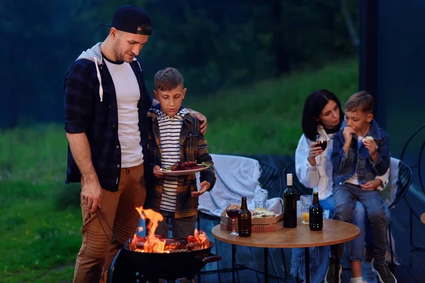 Glücklicher Vater und Sohn beim Grillen im Familienurlaub auf der Terrasse ihres modernen Hauses am Abend. — Stockfoto