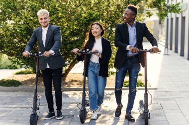 İş projesini tartışan çok ırklı ofis arkadaşları elektrikli scooterlarla ofis binasının yakınına gidiyorlar.
