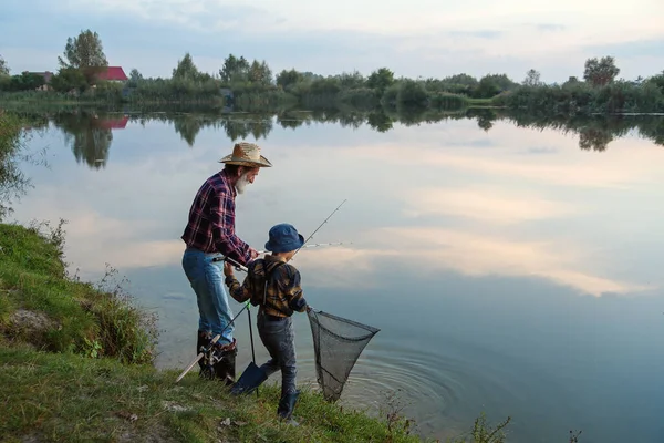 Χαριτωμένο 10χρονο αγόρι με τον έμπειρο γκρίζο-γενειοφόρο 70χρονο παππού του να πιάνει ψάρια στη λίμνη με δίχτυ προσγείωσης το ηλιοβασίλεμα. — Φωτογραφία Αρχείου