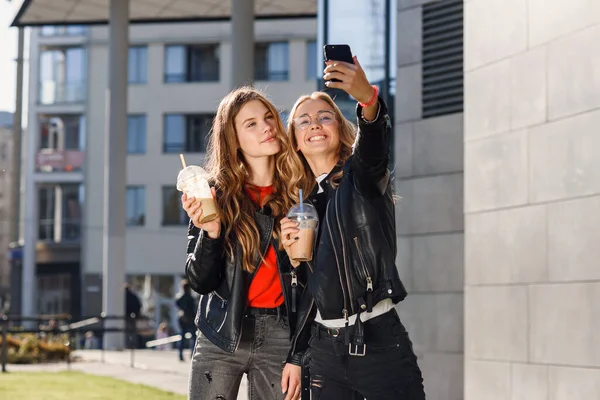 Duas elegantes meninas adolescentes atraentes com smoothie e smartphone perto de shopping center. Tempo de lazer com os melhores amigos. — Fotografia de Stock