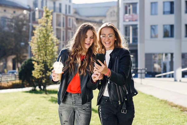 Duas elegantes meninas adolescentes atraentes com smoothie e smartphone perto de shopping center no centro da cidade. — Fotografia de Stock