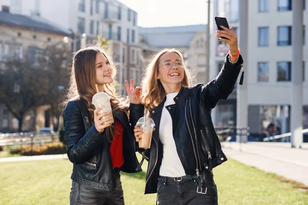 Duas elegantes meninas adolescentes atraentes com smoothie e smartphone fazendo selfie. Passar o lazer com os melhores amigos. — Fotografia de Stock