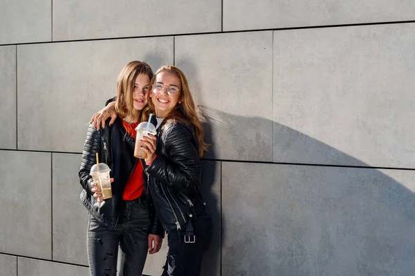 Duas lindas namoradas adolescentes com smoothie posando perto de parede de concreto cinza. Tempo de lazer com os melhores amigos. — Fotografia de Stock