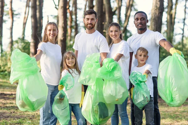 Active mixed race and multi age nature lovers show on camera plastic bags with rubbish that they picked up at the park.