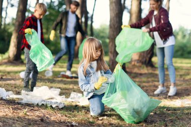 Motive olmuş güzel kız parktaki çok yaşlı gönüllülerin arka planında çöpleri topluyor. Kirliliğe karşı konsept