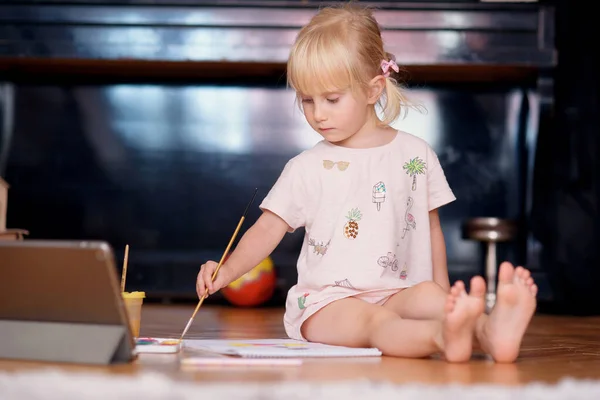 自宅の床に座って絵筆やカラフルな塗料で小さな面白い女の子の絵画。子供開発コンセプト. — ストック写真