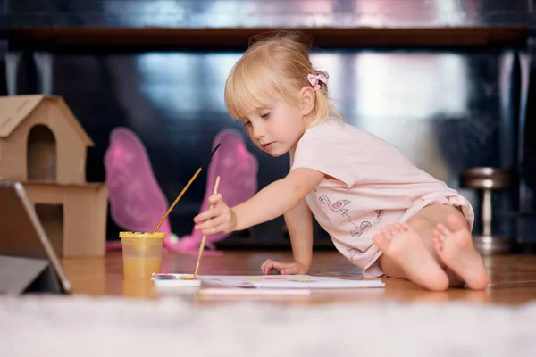 自宅の床に座って絵筆やカラフルな塗料で小さな面白い女の子の絵画。子供開発コンセプト. — ストック写真