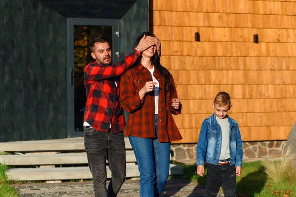 Homem feliz fecha os olhos de suas esposas com as mãos e a leva a um novo carro preto. Presente para mulher. — Fotografia de Stock