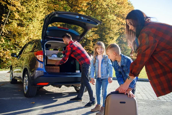 Joyful adorável jovem família carregando o tronco de automóveis por caixas de papelão e malas enquanto se muda para novo apartamento. — Fotografia de Stock