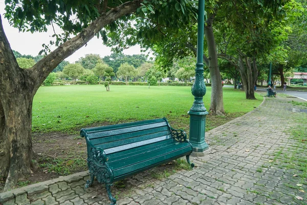 休日の緩和のための木の下で座って公園内の歩道に緑の木製のベンチ — ストック写真