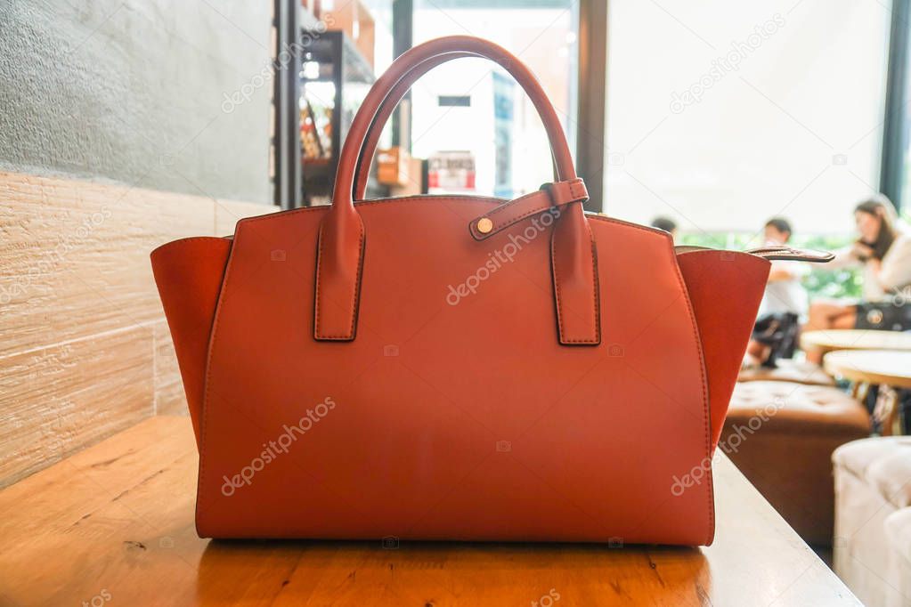 orange trendy handy leather fashionable women bag on wooden table in modern coffee cafe