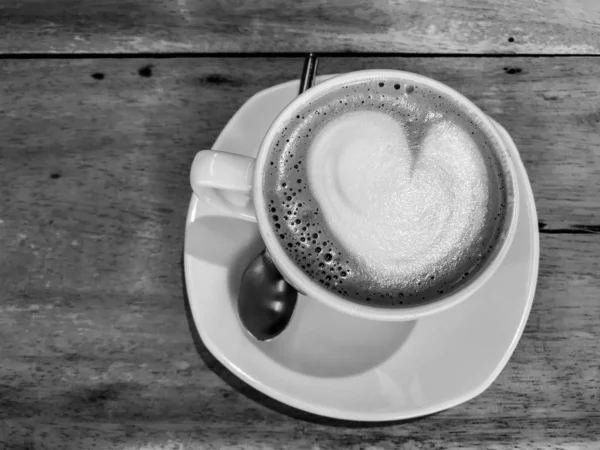 black and white color heart shape of latte art on hot coffee cup on wooden table in cafe