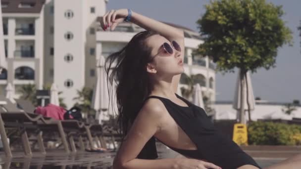 Piękna dziewczyna leży w basenie i sunbathes — Wideo stockowe