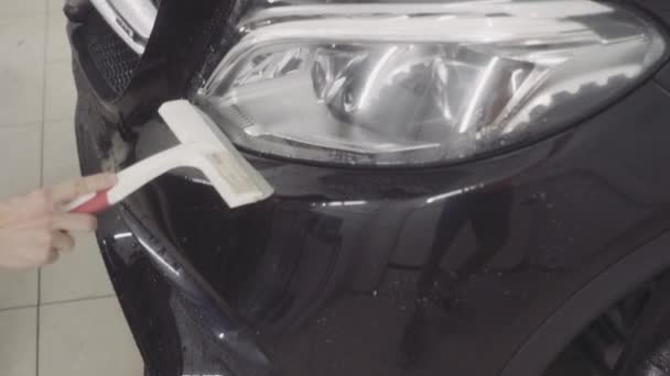 Un hombre lava la parte delantera del coche antes de aplicar una capa protectora sobre él — Vídeo de stock