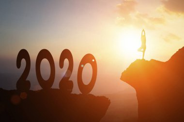 Genç kadınlar 2020 yılındaki yoga standında hedeflerine doğru meditasyon yaparken ve siluet doğal arka planda aktif bir şekilde uçurumun kenarında dururken. Özgürlüğü gösterir Mutlu yıllar Başarı ve sağlık konsepti.