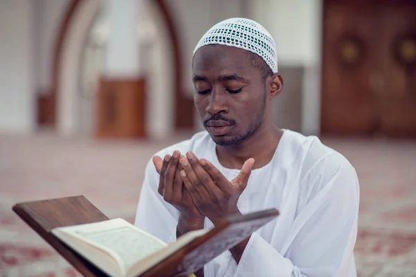 Negro africano musulmán hombre está orando en la mezquita con libro sagrado abierto del Corán —  Fotos de Stock
