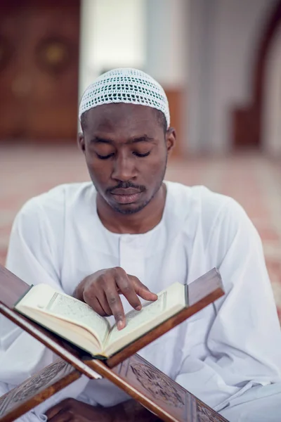 Negro africano musulmán hombre está orando en la mezquita con libro sagrado abierto del Corán —  Fotos de Stock