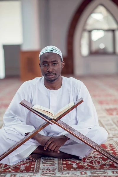 Negro africano musulmán hombre está orando en la mezquita con libro sagrado abierto del Corán —  Fotos de Stock