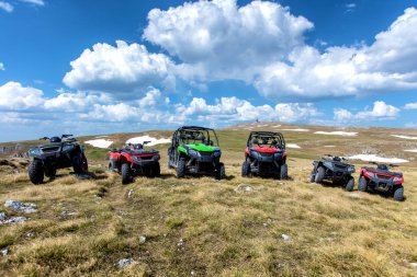 Parked ATV and UTV, buggies on mountain peak with clouds and blue sky in background clipart