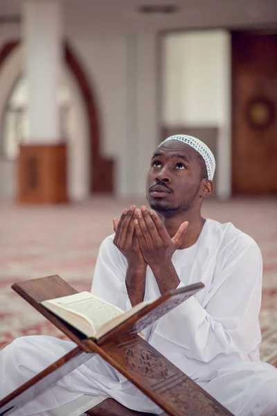 Black African Muslim Man Is Praying In The Mosque with open holy book of Koran