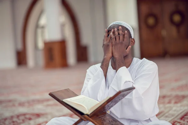 Negro africano muçulmano homem está orando na mesquita com aberto santo livro do Alcorão — Fotografia de Stock