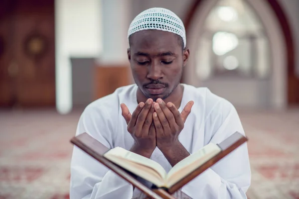 Negro africano muçulmano homem está orando na mesquita com aberto santo livro do Alcorão — Fotografia de Stock