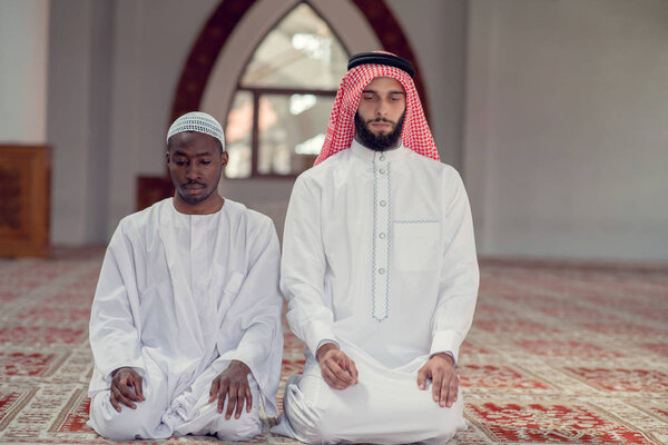 Two religious muslim man praying together inside the mosque.