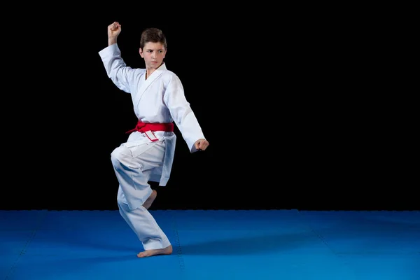 Młody chłopak ubrany w biały karate kimono z czerwonym pasem. — Zdjęcie stockowe