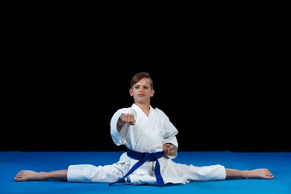 Karate niño vistiendo gi blanco y cinturón en un lado partido a horcajadas lado chino partido, con los brazos cruzados — Foto de Stock