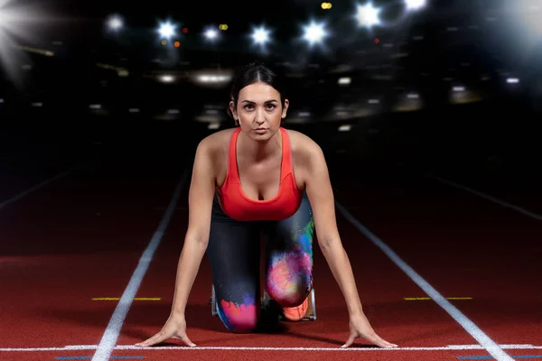 Woman sprinter leaving starting blocks on the athletic track. exploding start on stadium with reflectors — Stock Photo, Image