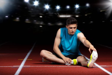 genç atletik erkek koşu parkuru üzerinde oturan ve spor stadyumunda germe