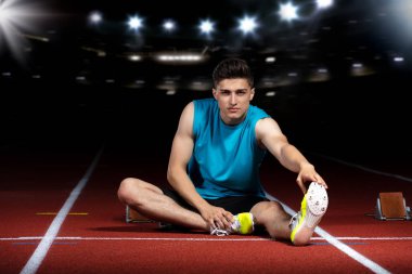 genç atletik erkek koşu parkuru üzerinde oturan ve spor stadyumunda germe