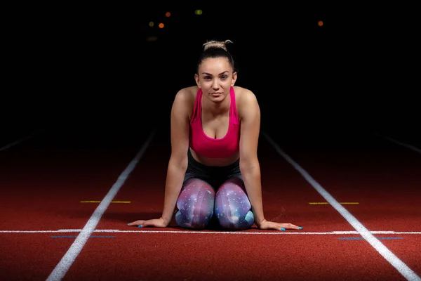Foto nocturna de mujer atlética sentada en pista de atletismo y descansando después del entrenamiento — Foto de Stock
