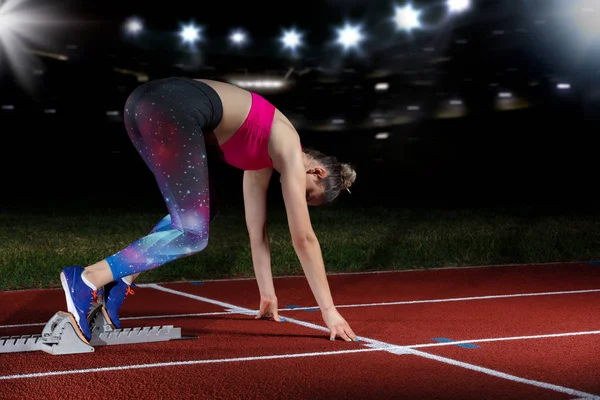 Mujer velocista dejando bloques de salida en la pista de atletismo. explosión de inicio en el estadio con reflectores — Foto de Stock