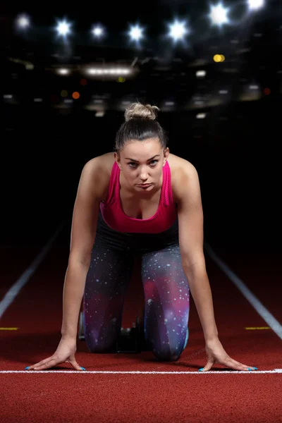 Mulher sprinter deixando blocos de partida na pista atlética. início explosivo no estádio com refletores — Fotografia de Stock