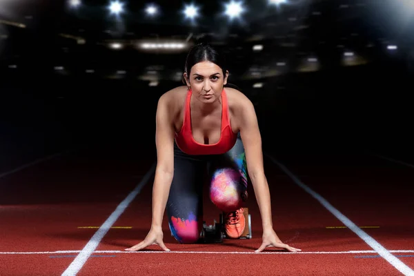 Woman sprinter leaving starting blocks on the athletic track. exploding start on stadium with reflectors — Stock Photo, Image