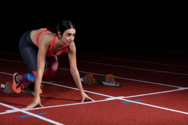 Kvinna sprinter lämna startblocken på athletic spår. exploderande start på stadion med reflektorer — Stockfoto