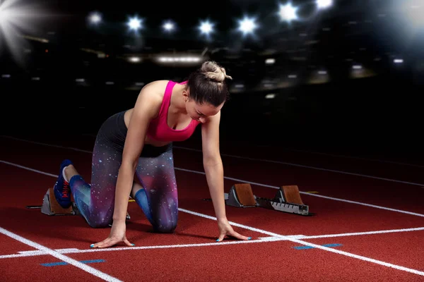 Žena sprinter opuštění startovací bloky na atletické dráze. explodující start na stadionu s reflektory — Stock fotografie