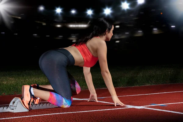 Mujer velocista dejando bloques de salida en la pista de atletismo. explosión de inicio en el estadio con reflectores — Foto de Stock