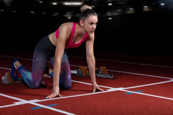 Mulher sprinter deixando blocos de partida na pista atlética. início explosivo no estádio com refletores — Fotografia de Stock