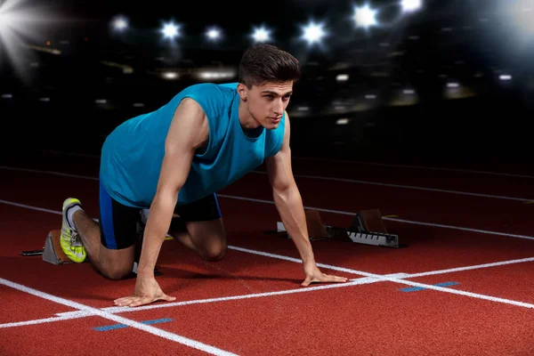 Sprinter leaving starting blocks on the running track in front of big modern stadium with lights. Explosive start. — Stock Photo, Image