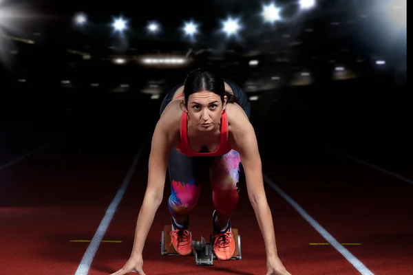 Kvinna sprinter lämna startblocken på athletic spår. exploderande start på stadion med reflektorer — Stockfoto