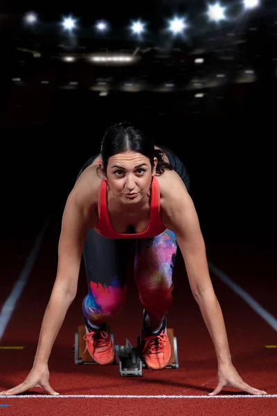 Woman sprinter leaving starting blocks on the athletic track. exploding start on stadium with reflectors — Stock Photo, Image