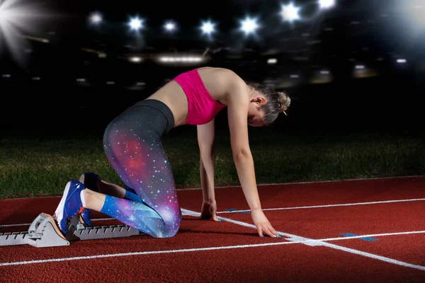 Woman sprinter leaving starting blocks on the athletic track. exploding start on stadium with reflectors — Stock Photo, Image