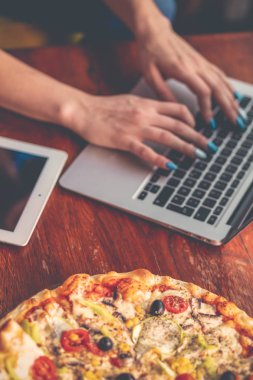 Masaüstü karışımı ofis aletleri, malzemeler ve ahşap ofis masasında pizza. Yukarıdan görüntüle.