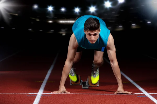 Sprinter deixando blocos de partida na pista de corrida em frente ao grande estádio moderno com luzes. Início explosivo . — Fotografia de Stock