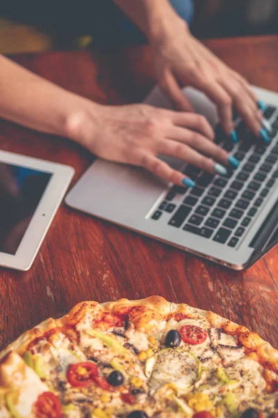 Desktop mix with office gadgets, supplies and pizza on a wooden office table background. View from above.